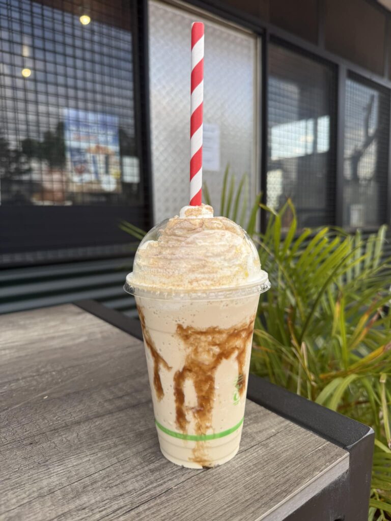Iced chai frappe topped with whipped cream and a sprinkle of cinnamon, served in a tall glass with a straw.